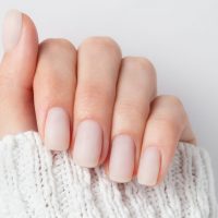 Matt nude nails close up o the light background. Winter manicure, woman hand in the warm sweater.